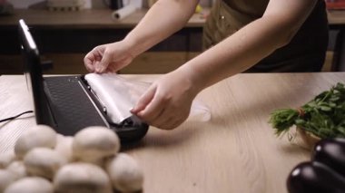 Ev mutfağındaki plastik poşetlere çiğ tavuk eti paketlemek için vakumlu mühür kullanan bir kadın. Uzun vadeli gıda korunması ve dondurulması için vakum ambalajlama süreci.