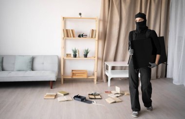 Siyah kar maskeli genç kadın hırsız gündüz vakti evden televizyon çalıyor. Boşluğu kopyala