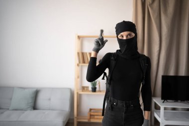 Kadın hırsız ya da siyah kar maskesi takmış hırsız evini soyuyor ve kameraya bakarken şok olmuş yüz ve fikir jesti yapıyor. Boşluğu kopyala