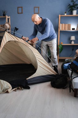 Yaşlı gezgin içeride çadır kuruyor, kamp, yürüyüş ya da keşif gezisinden önce çadır parçalarını kontrol ediyor. Boşluğu kopyala