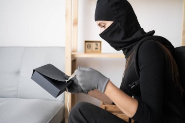 Hırsızlık, hırsızlık ve suç kavramı. Siyah kar maskeli bir kadın hırsız evden ve suç mahallinden para çalıyor. Boşluğu kopyala