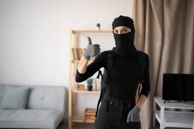 Hırsız, hırsız ve hırsız. Siyah kar maskesi ve eldiven giyen genç bir kadın birinin evine el hareketi yapıyor gibi görünüyor. Boşluğu kopyala