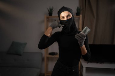 Siyah kar maskesi takan kadın hırsız bana telefon işareti yapıp kameraya para veriyor. Hırsızlık, suç ve soygun..