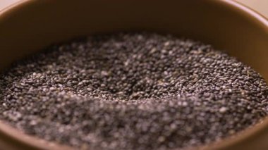 Chia tohumları ahşap kaseye dökülüyor, makro manzaralı. Yakın plan.