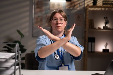 Nurse looking at camera confident gesture sign stop with crossed hands, no negative, on night shift in the hospital. healthcare concept