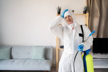 Evde çalışan haşere kontrol servisinden kadın ilaçlamacı ellerini başının üstüne koyuyor ve evde negatif duygu ifadesi sergiliyor. Boşluğu kopyala