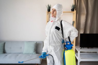 Haşere ilaçlama servisinden kadın ilaçlayıcı sprey şişesiyle evin içinde çalışıyor. Kaslarına dokunurken, sırt ağrısı çekerken, evde sırt ağrısı çekerken.