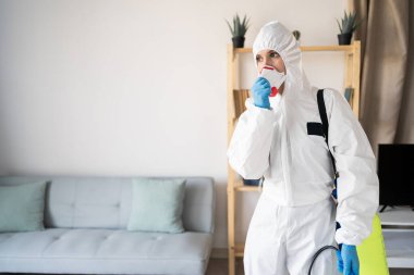 Evde solunum maskesi takan böcek ilaçlama servisinden kadın ilaçlamacı evin içinde çalışıyor. Boşluğu kopyala