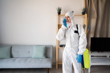 Evde ilaçlama servisinden kadın ilaçlamacı sprey şişesiyle çalışıyor evde bağırarak anons yapıyor. Boşluğu kopyala