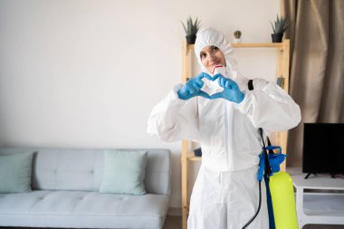 Evde sprey şişesiyle çalışan haşere ilaçlama servisinden kadın ilaçlamacı kendini mutlu hissediyor ve evde kalp hareketlerini romantik şekillendiriyor. Boşluğu kopyala