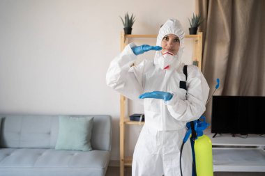 Evde çalışan haşere ilaçlama servisinden kadın ilaçlayıcı sprey şişesiyle evde elleri olan büyük bir nesne gösteriyor. Boşluğu kopyala