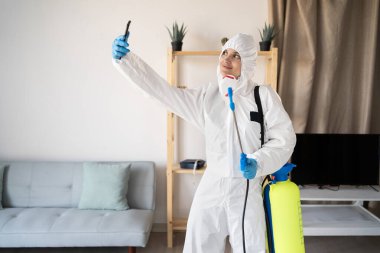 Evde ilaçlama şişesiyle çalışan haşere ilaçlama servisinden kadın ilaçlamacı evde akıllı telefondan kendi portresini yapıyor. Boşluğu kopyala