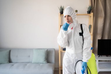 Hastalık konsepti. Evde çalışan böcek ilaçlama servisinden kadın ilaçlamacı. Öksürük ilacı şişesiyle çalışıyor. Evde grip belirtileri var.