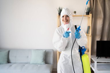 Evin içinde çalışan haşere ilaçlama servisinden kadın böcek ilaçlayıcı sprey şişesiyle evde seni seçen kamerayı işaret ediyor. Boşluğu kopyala