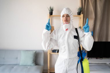 Haşere ilaçlama servisinden kadın ilaçlamacı evin içinde sprey şişesiyle çalışıyor parmaklarını çapraz yapıp evde istenilen dileği diliyor.