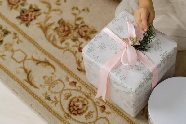 小さな手は美しい白い紙に包まれたクリスマスプレゼントにピンクのリボンを保持します クリスマスお祝いのコンセプト — ストック写真