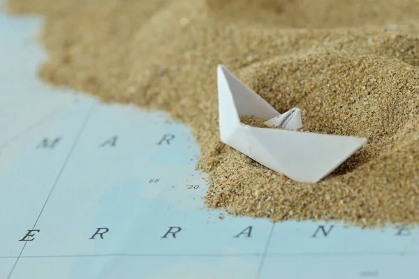 stock image Overturned paper boat on a map with sand - Immigration concept