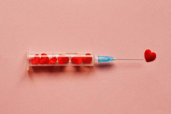 Syringe full of hearts on pink background - Love concept