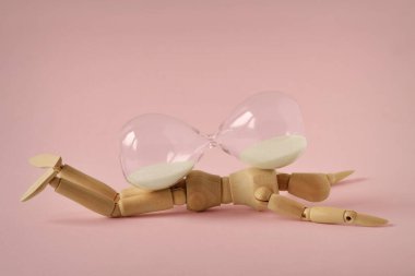 Pembe arka planda kum saatinin altında yatan tahta manken zamanı, sağlığı ve yaşlanmayı durdurma kavramı