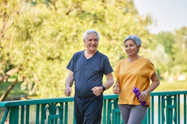 アジアと白人の古い妻と夫は夏の公園で橋に沿って散歩を積極的に着用し 一緒に外で朝のスポーツ散歩をお楽しみください 健康的なライフスタイルと退職 — ストック写真