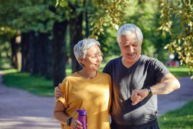 Yaz parkında spor yapan yaşlı bir çift, sağlığa önem veren uygulamaları kullanarak saat kontrol verileri takıyor. Aktif sportif, emekli eşler modern teknoloji kavramını kullanarak yaşam tarzını değiştiriyor.