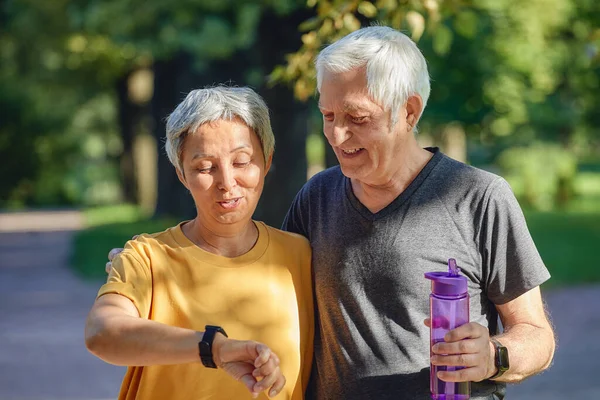 高齢者のカップルは 健康を気にするアプリケーションを使用して夏の公園の摩耗チェックデータで動作します 現代的な技術の概念を使用してアクティブなスポーティ引退した配偶者のライフスタイル — ストック写真
