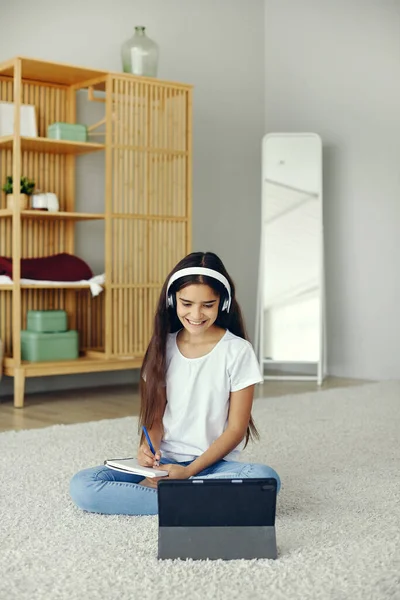 12岁以下的漂亮女孩戴着无线耳机 坐在地板上听音频课程学习 在家学习使用数字平板电脑 现代技术应用于电子学习 基因Z新技能获取 — 图库照片