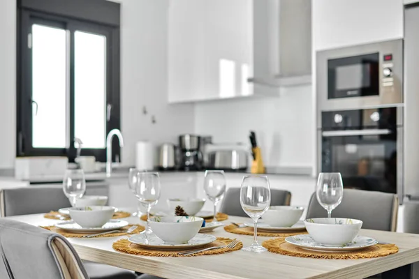 現代的なファッショナブルな居心地の良いキッチンの空のワイングラスとディナーウェアでは ダイニングテーブルで提供されるランチの準備ができています — ストック写真