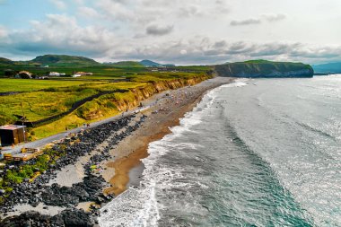 Atlantik Okyanusu 'nun kıyısında turistlerin dinlendiği kayalık kıyı şeridi ve kumlu plaj. Bulutlu bir gökyüzü. Sao Miguel Adası, Azores, Portekiz. Seyahat ve turizm, yaz tatili konsepti.