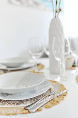 Akşam yemeği için beyaz porselen sofra takımlarını paspaslara ve boş şarap kadehlerine koyun. Masa ayarları evde ya da restoranda misafirleri bekler. Dekorasyon için suni saksı, insan olmaz.