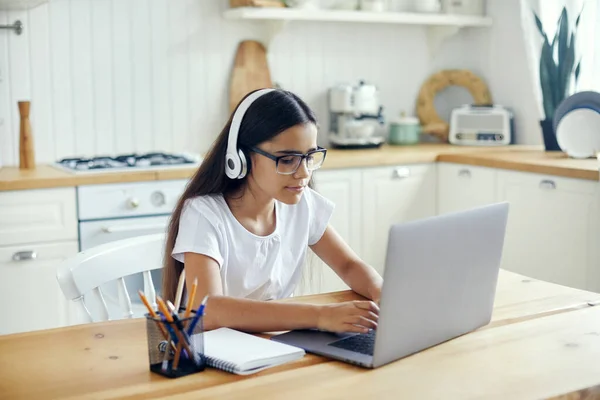 Pre-teen 12s girl in headphones and eyeglasses sit at table e-learns, listen online course, audio lesson, get new knowledge, skills using internet and modern tech. Development, education, eye-sight