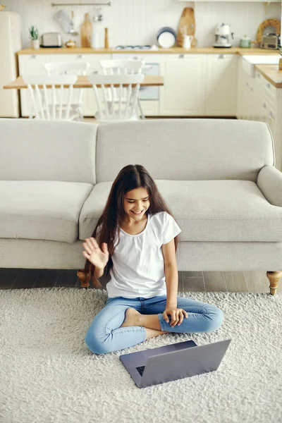 Attractive middle-eastern ethnicity pre-teen 12s girl sit on floor in living room wave hand greeting friend start videocall event use modern laptop. Virtual meeting, worldwide communication, blogging