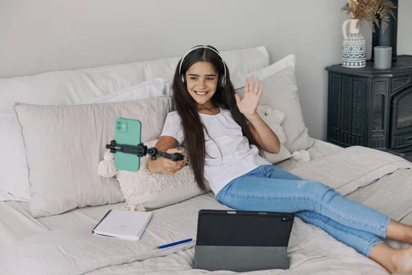 迷人的十多岁前女孩抱着自拍棒躺在床上拍照 为社交媒体频道录制视频 参加流媒体直播 在网上消闲 Vlogging Fun 图库图片