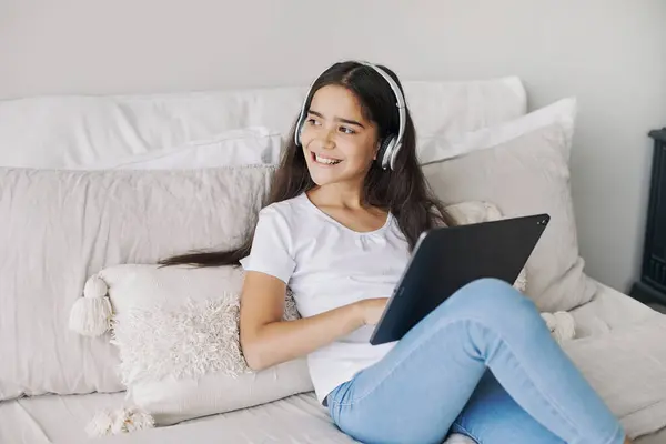 迷人的12岁前女孩穿着无线耳机 坐在舒适的卧室里 使用现代数码平板电脑 我为娱乐 教育和休闲而创造和使用技术 免版税图库照片