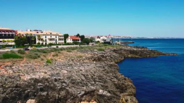 Ponta Delgada kasabasının kıyı manzarası, kayalık arazi, mavi okyanus suları, kıyıya paralel uzanan yol, uzaklarda tekneleri ve kırmızı feneri olan marina bölgesi. San Miguel Adası, Azores