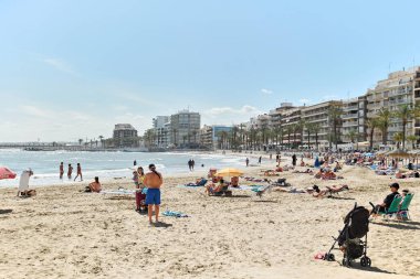 Torrevieja, İspanya - 19 Nisan 2024: Torrevieja şehrinin kumsal sahili. Del Cura 'da güneşlenen bir sürü insan var. Costa Blanca, Alicante, İspanya. Seyahat yeri ve turistik yerler