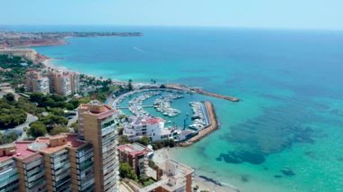 İHA bakış açısına göre İspanyol turistler güneşli yaz günlerinde Dehesa de Campoamor köyü manzarasına, liman manzarasına, kıyı gökdelenlerine ve Akdeniz manzarasına sahipler. Costa Blanca 'da. İspanya