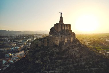 Engebeli tepenin tepesindeki Monteagudo heykeli, gün batımına bakan şehir manzarası. Antik kale ve çevreleyen manzara. Kültür ve tarihi sembol. Murcia, Alicante ili. İspanya