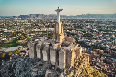 Engebeli tepenin tepesindeki Monteagudo heykeli, gün batımına bakan şehir manzarası. Antik kale ve çevreleyen manzara. Kültür ve tarihi sembol. Murcia, Alicante ili. İspanya