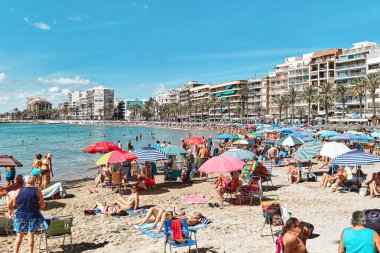 Torrevieja, İspanya - 28 Eylül 2024: Güneşli bir sonbahar gününde insanlar Playa Del Cura plajında güneşleniyor. Seyahat yerleri kavramı. Torrevieja, Alicante ili, Costa Blanca, İspanya