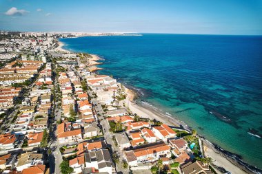 Hava aracı bakış açısı, güneşli bir günde Torre de la Horada kasabası, konut evleri manzarası ve Akdeniz turkuaz suları. Tatil köyü. Alicante ili, İspanya