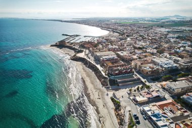 Hava aracı bakış açısı, güneşli bir günde Torre de la Horada kasabası, konut evleri manzarası ve Akdeniz turkuaz suları. Tatil köyü. Alicante ili, İspanya