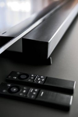 Modern ses çubuğuna yakın çekim ve karanlık yüzeyde iki adet parlak siyah uzaktan kumanda. Minimalist ev eğlencesi kurulumu yüksek teknoloji ses donanımı ve şık tasarım, insan yok.