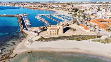 İspanyol Akdeniz kıyısındaki modern marina yakınlarındaki tarihi Torre de la Horada gözlem kulesinin hava manzarası kültürel miras, sahil mimarisi ve manzaralı kıyı güzelliğini birleştiriyor. İspanya