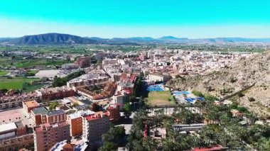 Palmeral de Orihuela 'nın ya da palmiye koruluğunun havadan görünüşü, açık İspanyol gökyüzü altında kentsel yayılma ve dağlık zemin arasında yemyeşil bir vaha. Costa Blanca, Alicante Eyaleti