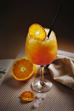 Ezilmiş buz, kurutulmuş portakal dilimi ve samanla servis edilen canlı turuncu kokteyl..