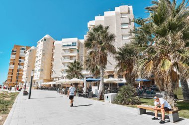Torrevieja, Spain - September 28, 2024: Street view of seaside promenade in Torrevieja, with palm trees, residential buildings, outdoor cafes, tourists enjoy sunny day near Mediterranean coast