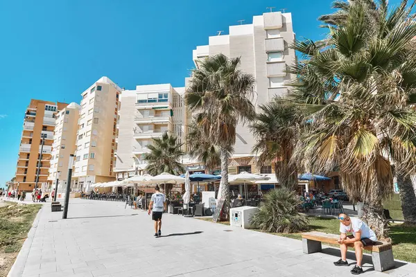 Torrevieja, Spain - September 28, 2024: Street view of seaside promenade in Torrevieja, with palm trees, residential buildings, outdoor cafes, tourists enjoy sunny day near Mediterranean coast