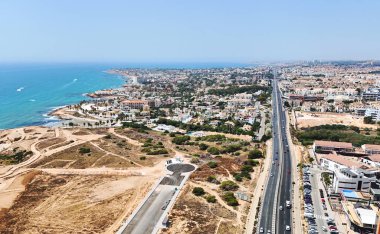 Costa Blanca 'daki Playa Flamenca' nın varsayılan panoramik hava manzarası Akdeniz kıyı şeridi, kumlu plajlar, konut evleri, oteller ve sahil kasabası boyunca uzanan yoğun bir kıyı yolu gösteriyor.