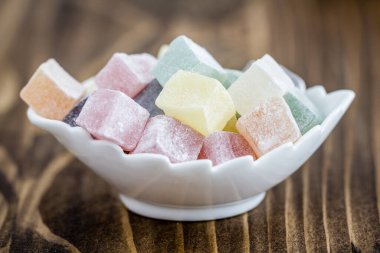 Colorful Turkish delight in white bowl on wooden background, rustic presentation of multicolored cube shaped sweets.